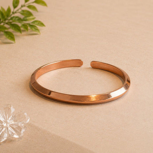 Rose gold bangle on a beige surface with a plant and crystal in the background