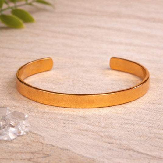 Gold bangle on a textured beige surface with a blurred green plant in the background