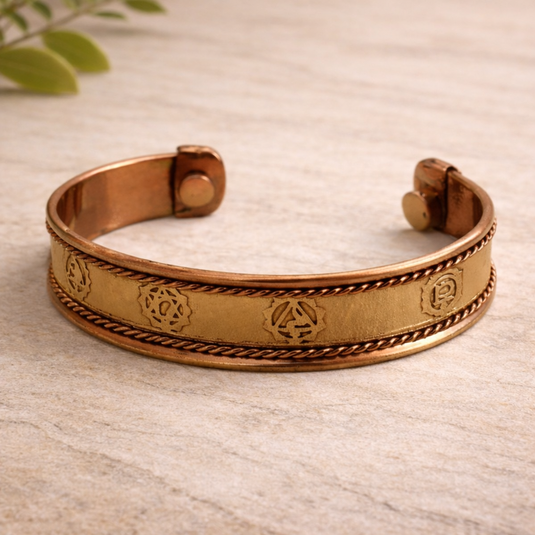 Copper bracelet with engraved designs on a light wooden surface