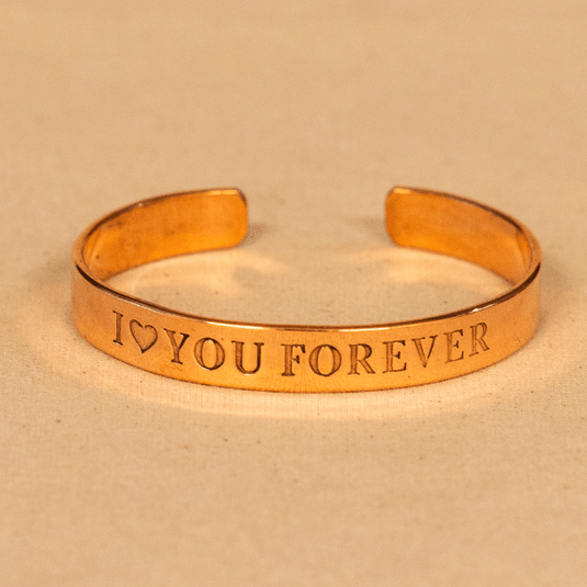 Gold bracelet with 'I ❤️ YOU FOREVER' engraving on a beige background