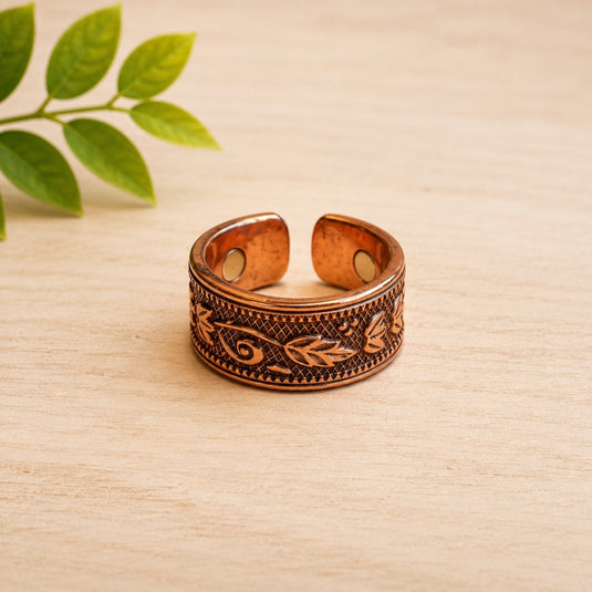 Copper bracelet with intricate designs on a beige surface with green leaves in the background