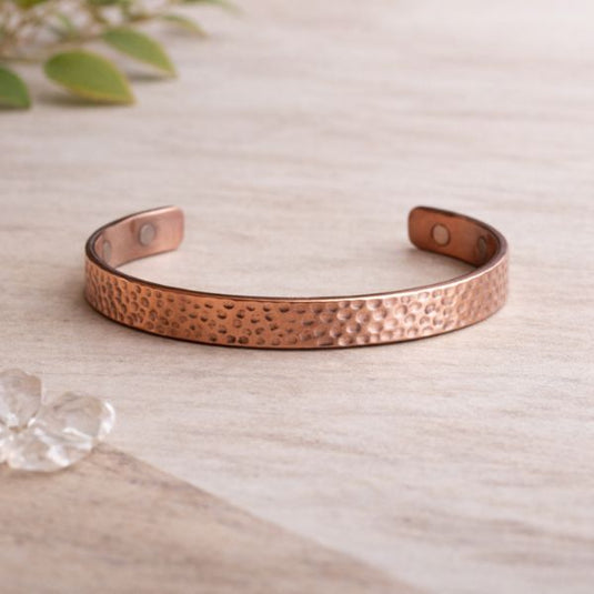 Hammered copper bracelet on a light wooden surface with a blurred plant in the background