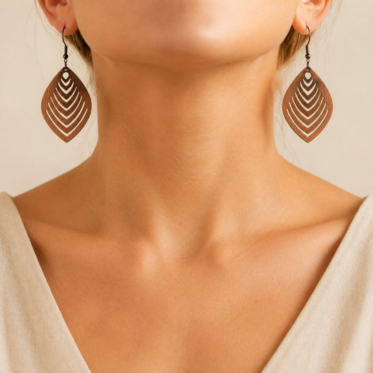 Close-up of a woman's neck and lower face wearing large teardrop-shaped wooden earrings with concentric cutout patterns in brown and beige tones.