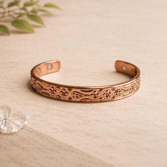 Decorative copper bracelet on a wooden surface with a plant in the background