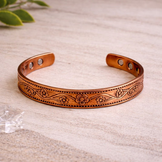 Copper bracelet with floral patterns on a light wooden surface