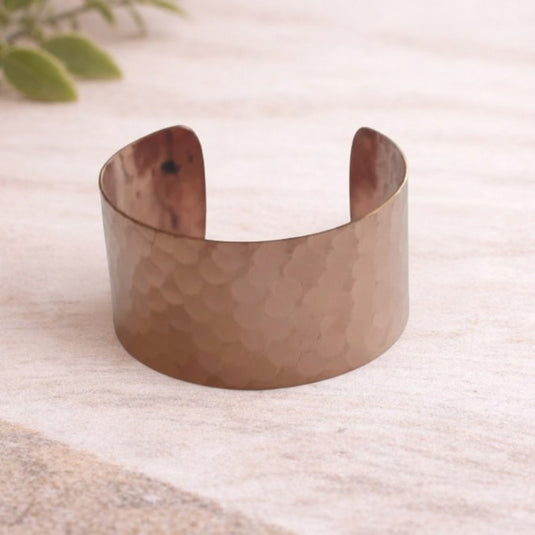 Hammered copper bracelet on a textured surface with a blurred plant in the background