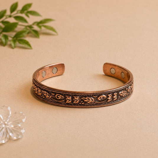 Decorative copper bracelet on a beige surface with a plant in the background