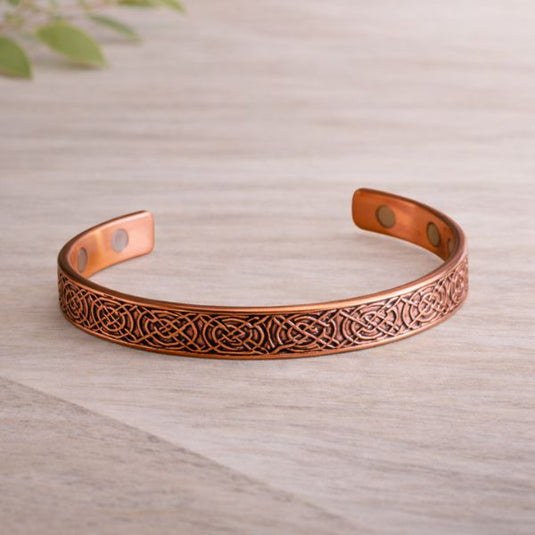 Copper bracelet with intricate design on a wooden surface
