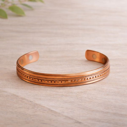 Copper bracelet with intricate design on a light wooden surface
