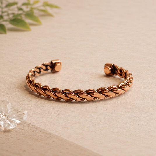 Rose gold braided bracelet on a beige surface with a soft focus background