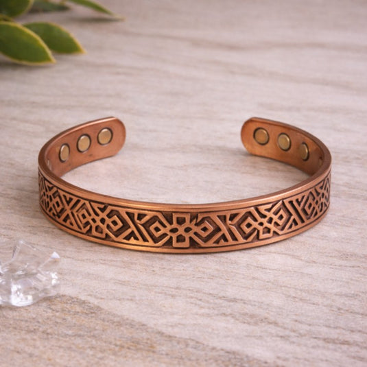 Copper bracelet with intricate design on a light wooden surface