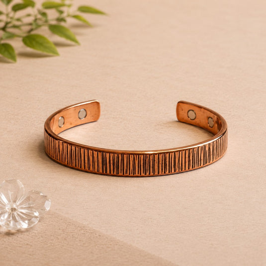 Copper bracelet on a beige surface with a plant in the background