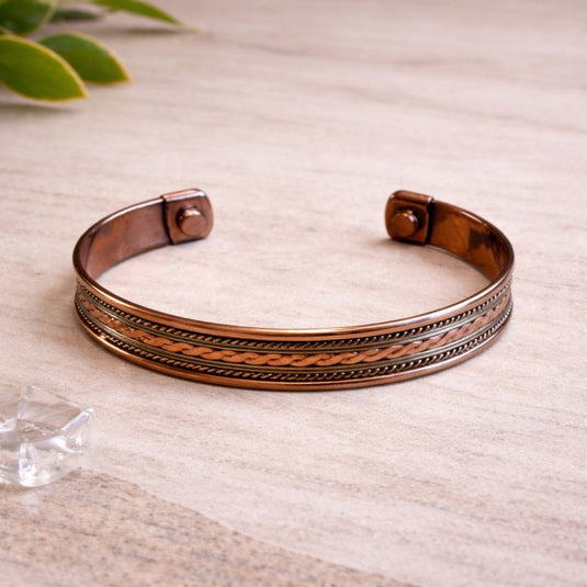 Copper bracelet on a light wooden surface with a plant in the corner