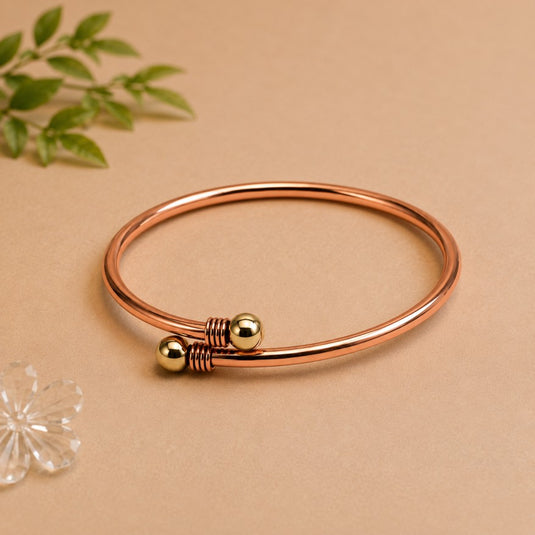 Rose gold bracelet with a gold bead on a beige background