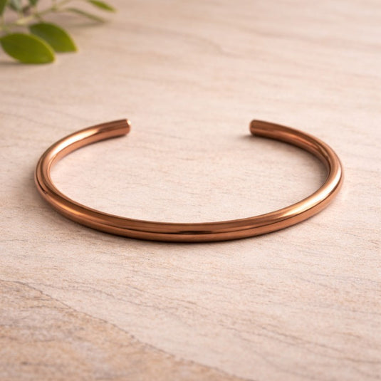 Rose gold bracelet on a light wooden surface with a blurred green leaf in the background