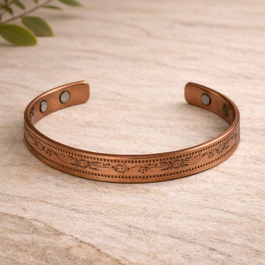 Copper bracelet with engraved design on a light wooden surface