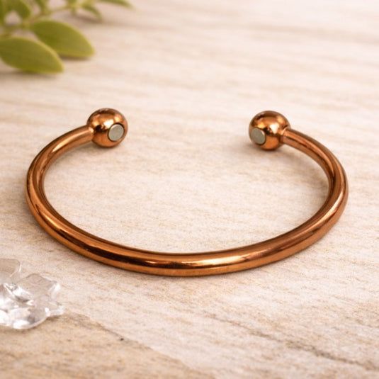 Rose gold bracelet on a light wooden surface with a blurred green plant in the background