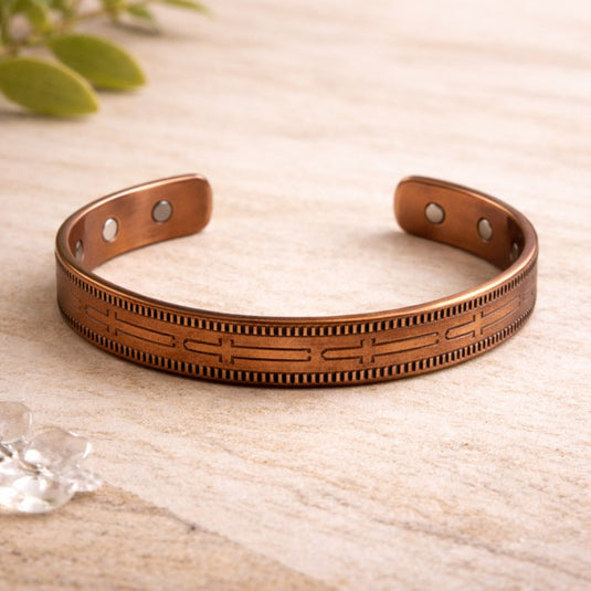 Bronze bracelet on a light wooden surface with a plant in the background