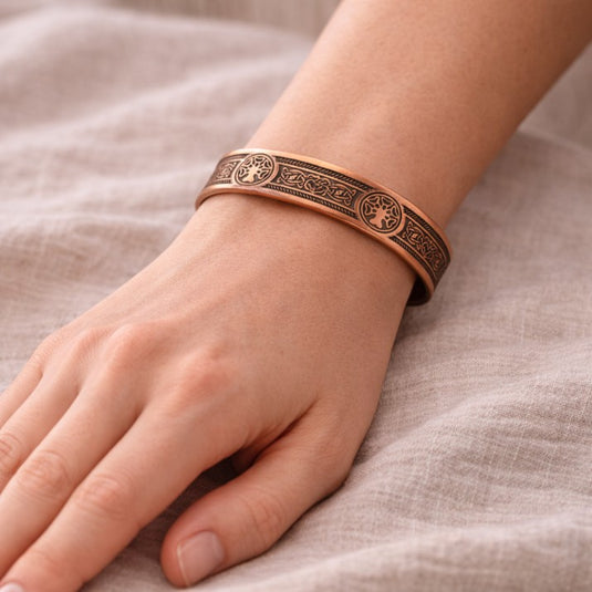Copper bracelet with intricate designs on a wrist against a neutral background