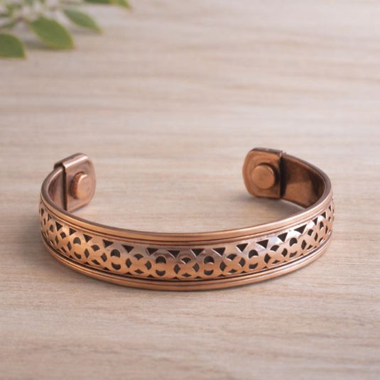 Copper bracelet with intricate design on a light wooden surface