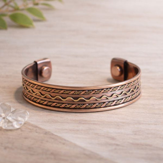 Copper bracelet with intricate designs on a light wooden surface.