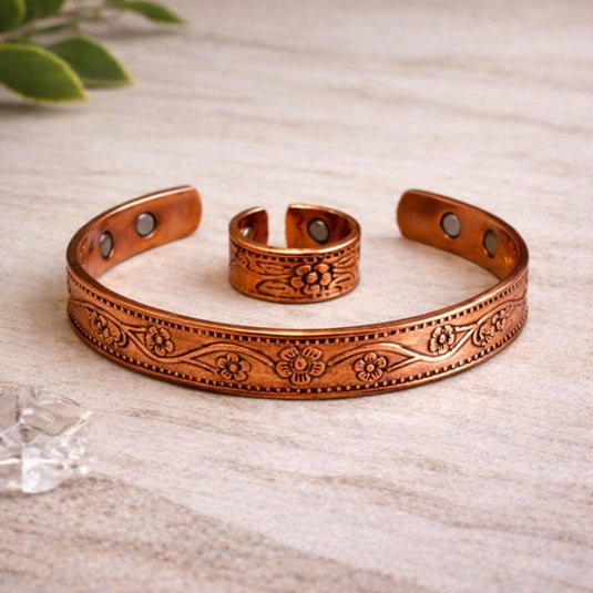 Copper bracelets with floral patterns on a light wooden surface.