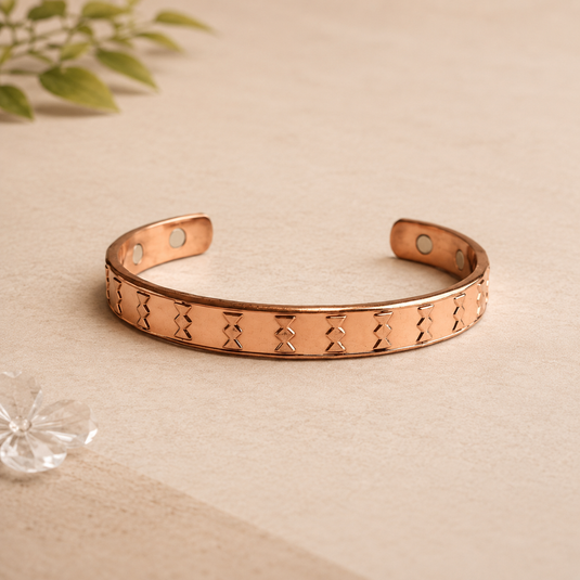 Rose gold bracelet on a beige surface with a plant in the background