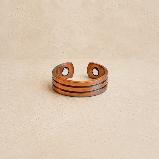 A wooden cuff bracelet with three horizontal grooves and circular magnetic snap closures, displayed on a textured beige surface.
