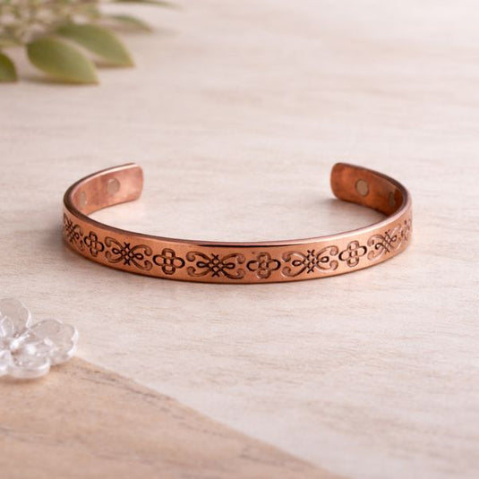 Copper bracelet with engraved design on a light wooden surface