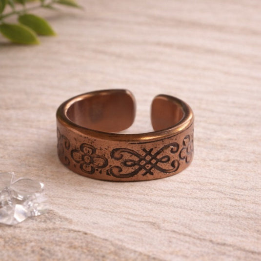 Bronze adjustable ring with intricate design on a light wooden surface